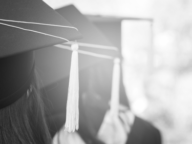 Black and white image, view from behind of students with cap and gown on