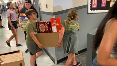 Two students carrying a box full of cereal boxes