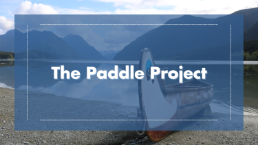Paddle Project Cover Image Scenic image of water and mountains with a canoe at shore. Blue overlay with title "The Paddle Project".