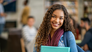 Smiling Highschool Student Smiling female student holding a binder with a backpack on