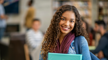 Smiling female student holding a binder with a backpack on