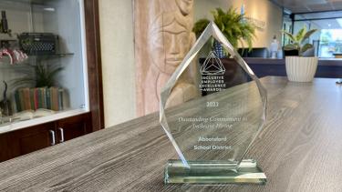 Outstanding Commitment to Inclusive Hiring Clear glass award sits on table with front reception of district building in background
