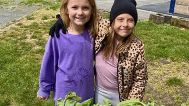 Two elementary female students stand in front of fresh radishes from the garden