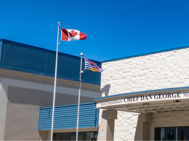 Canadian and British Columbia flags flying in front of Chief Dan George Middle School on a clear blue day.