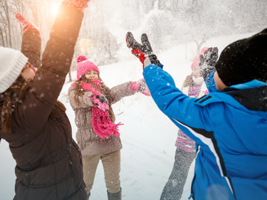 Children in winter clothing playing outdoors in the snow, tossing snow into the air during a snowy winter day.