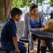 Female secondary student reads book to male elementary student