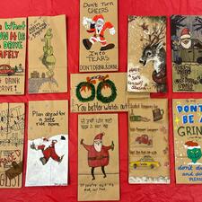 Paper bags laying flat on a red background. Bags have Christmas themed drawings on them.