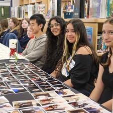 Students sitting at table, ready to hand out photos and certificates