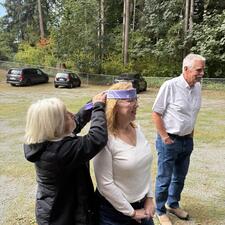 One female wraps and tying a bandana around another female's head with a man standing off to the side.